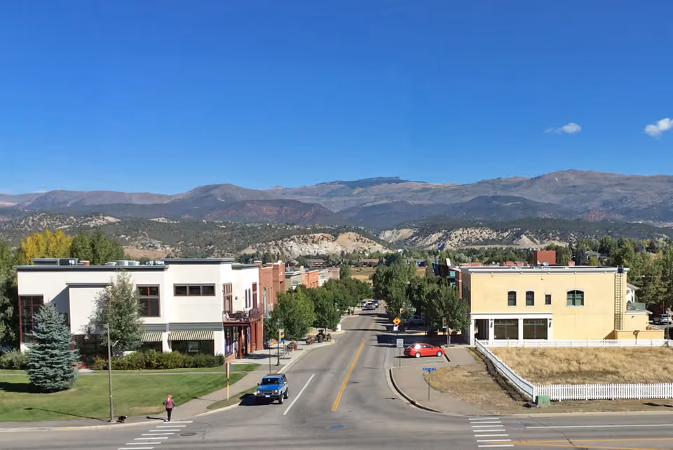 A street view with a row of low-rise buildings and distant mountains under clear blue sky.