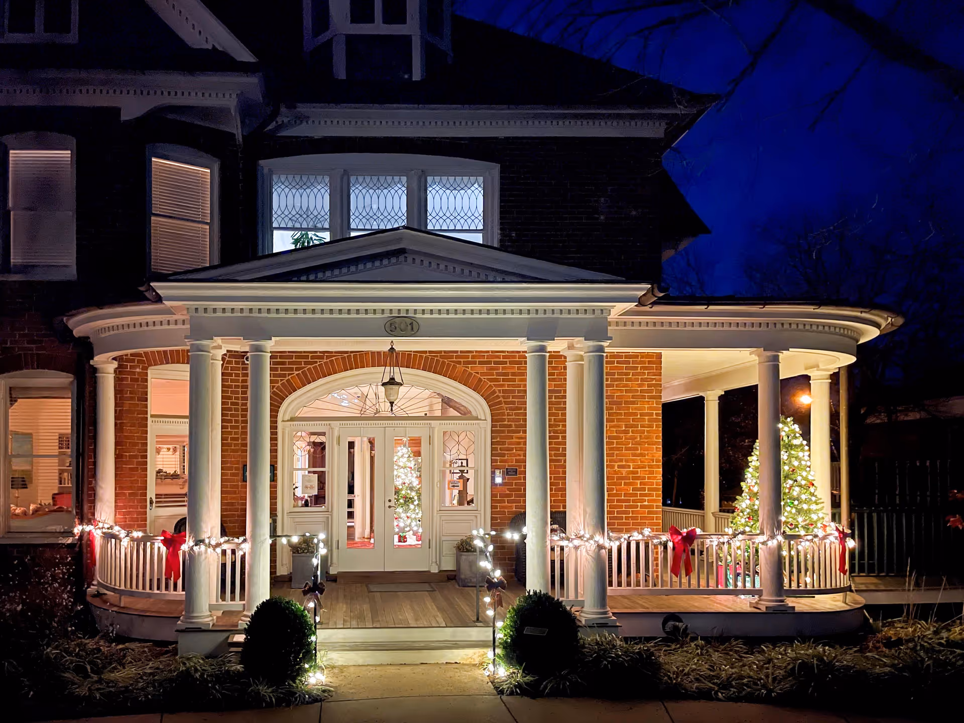 Night view of a brick hospice house with a lit, decorated front porch.