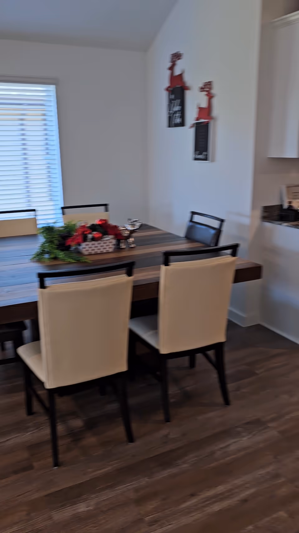 Dining room with wooden table, beige chairs, holiday centerpiece, and adjacent kitchen area.