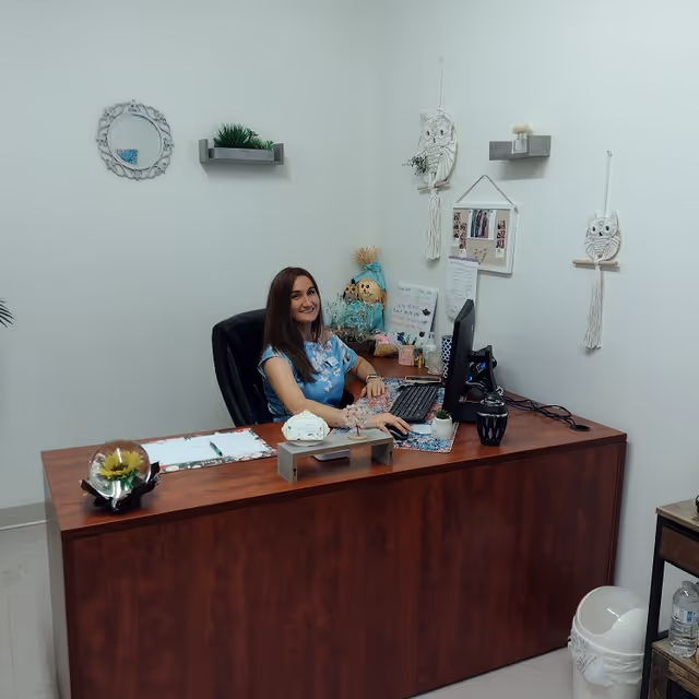 A smiling receptionist sits at a wood desk with computer in a cozy office.