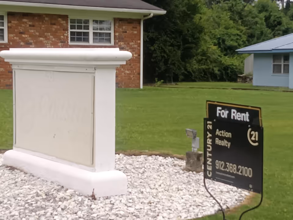 Front exterior of a brick building with a 'For Rent' sign on a lawn.