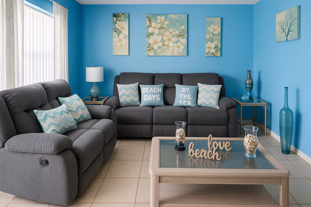 Turquoise living room featuring two gray reclining sofas with patterned pillows, coastal wall art, and a glass-top coffee table with beach-themed decor.