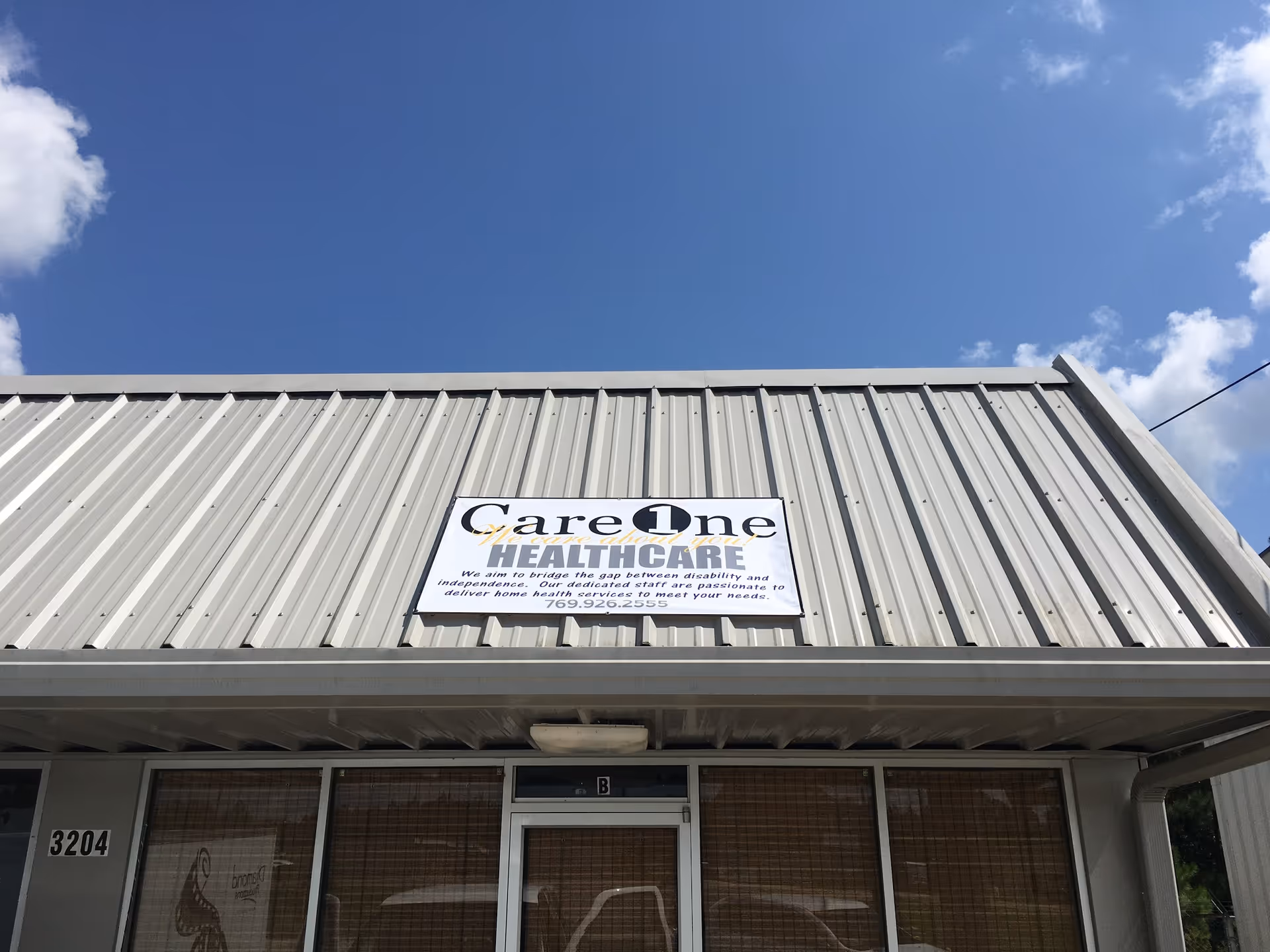 Metal-siding senior care facility storefront with sign and glass entrance under blue sky.