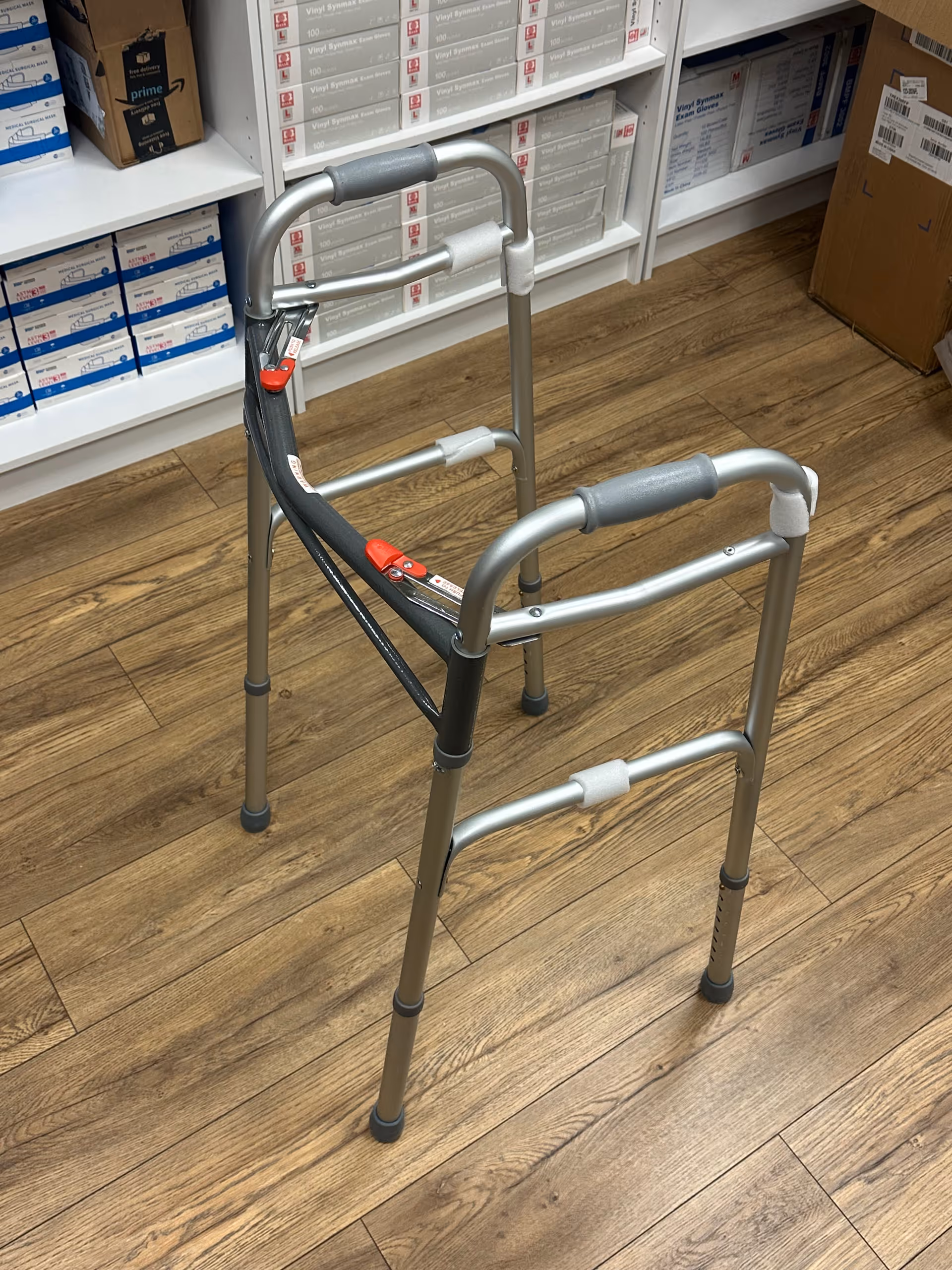 A metal walker stands in a storage area with shelves and wood flooring.