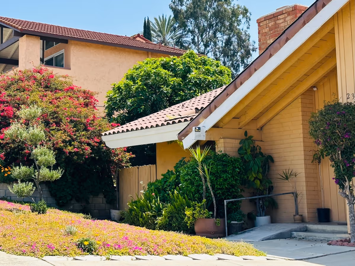 Exterior view of a beige senior living facility with a tiled roof and garden.