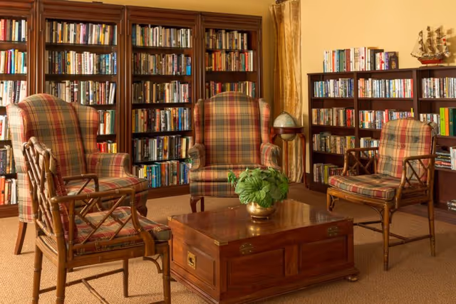 Cozy reading room with plaid armchairs arranged around a wooden coffee table and bookshelves lining the walls.