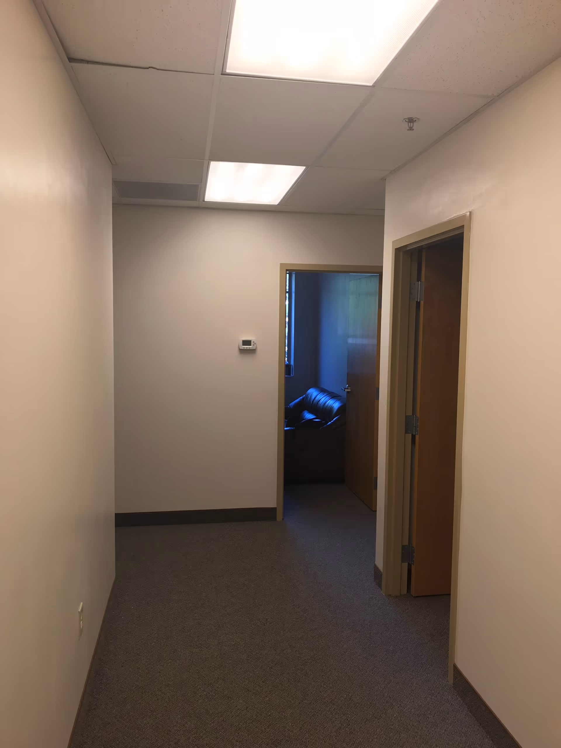 Empty corridor in Kind Hearts Senior Care, doorway reveals a dark sofa.