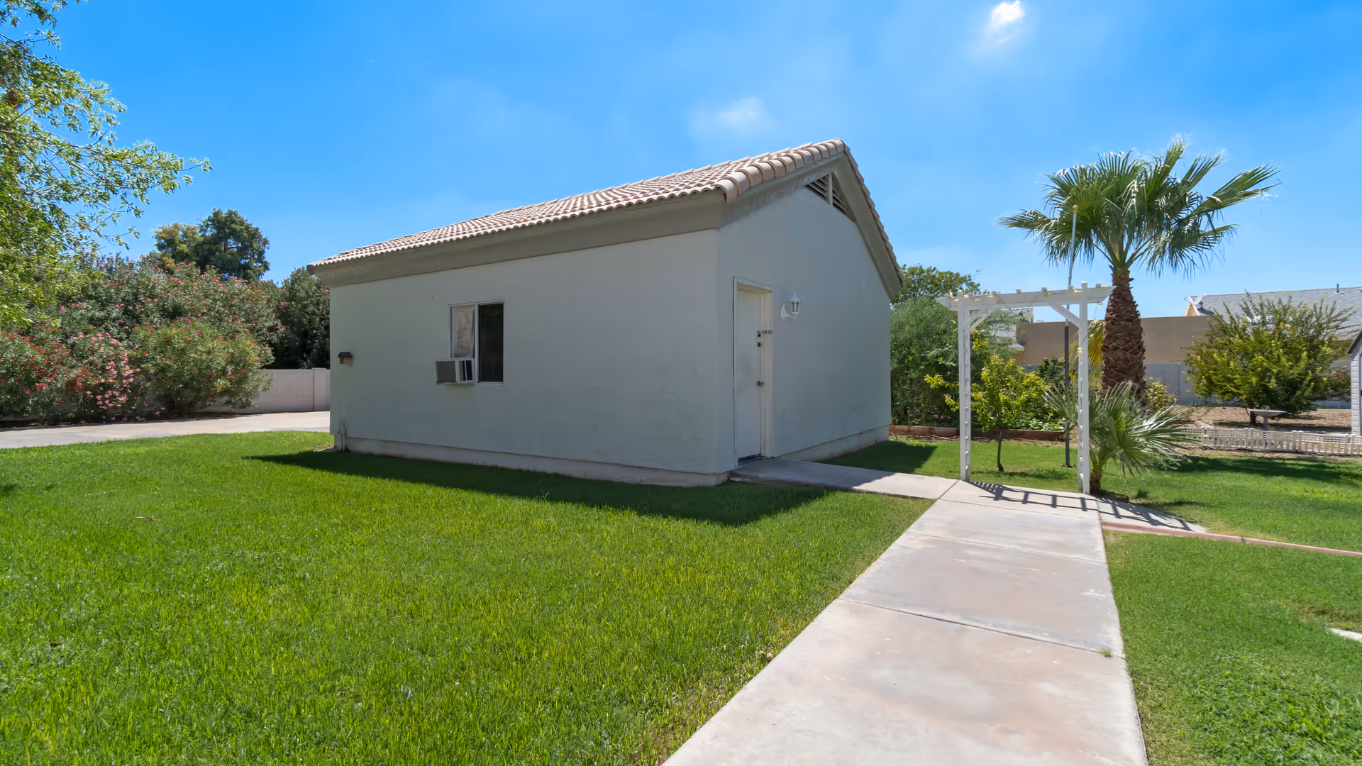 A small light-blue building with tiled roof, green lawn, and a concrete walkway.