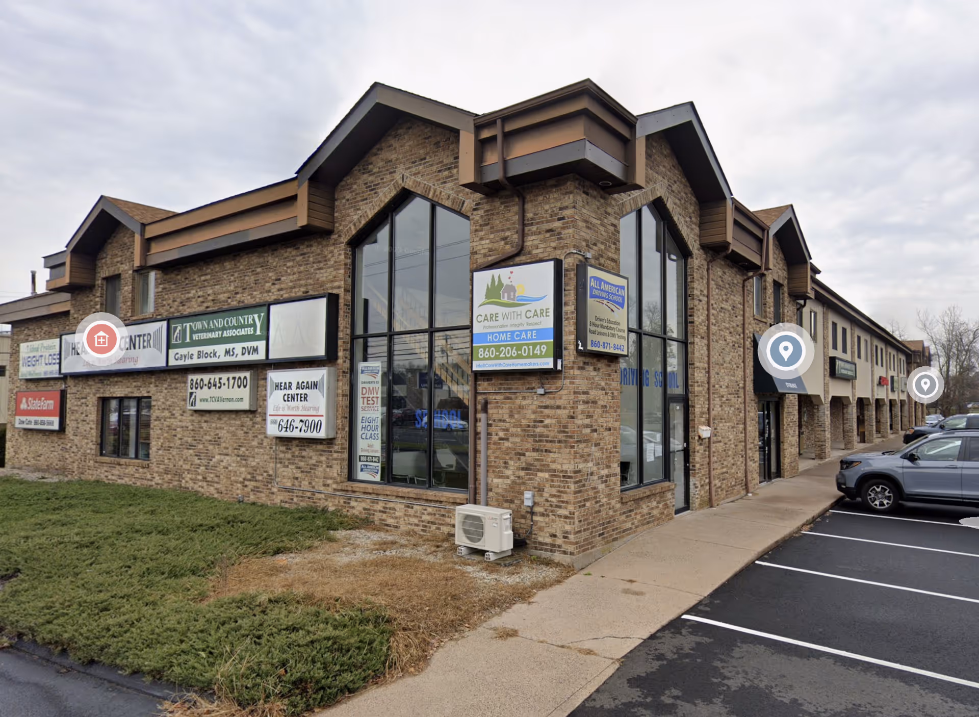 Brick strip mall exterior with storefront windows, signs, and a paved parking lot.