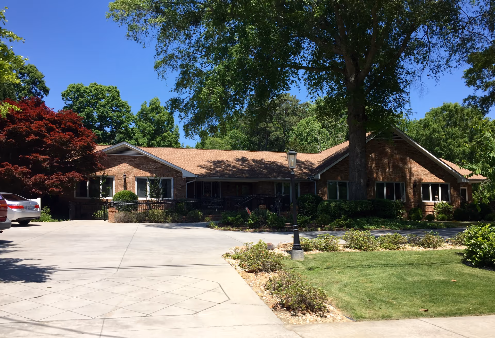Brick senior living facility exterior with parking area, trees, and landscaping.