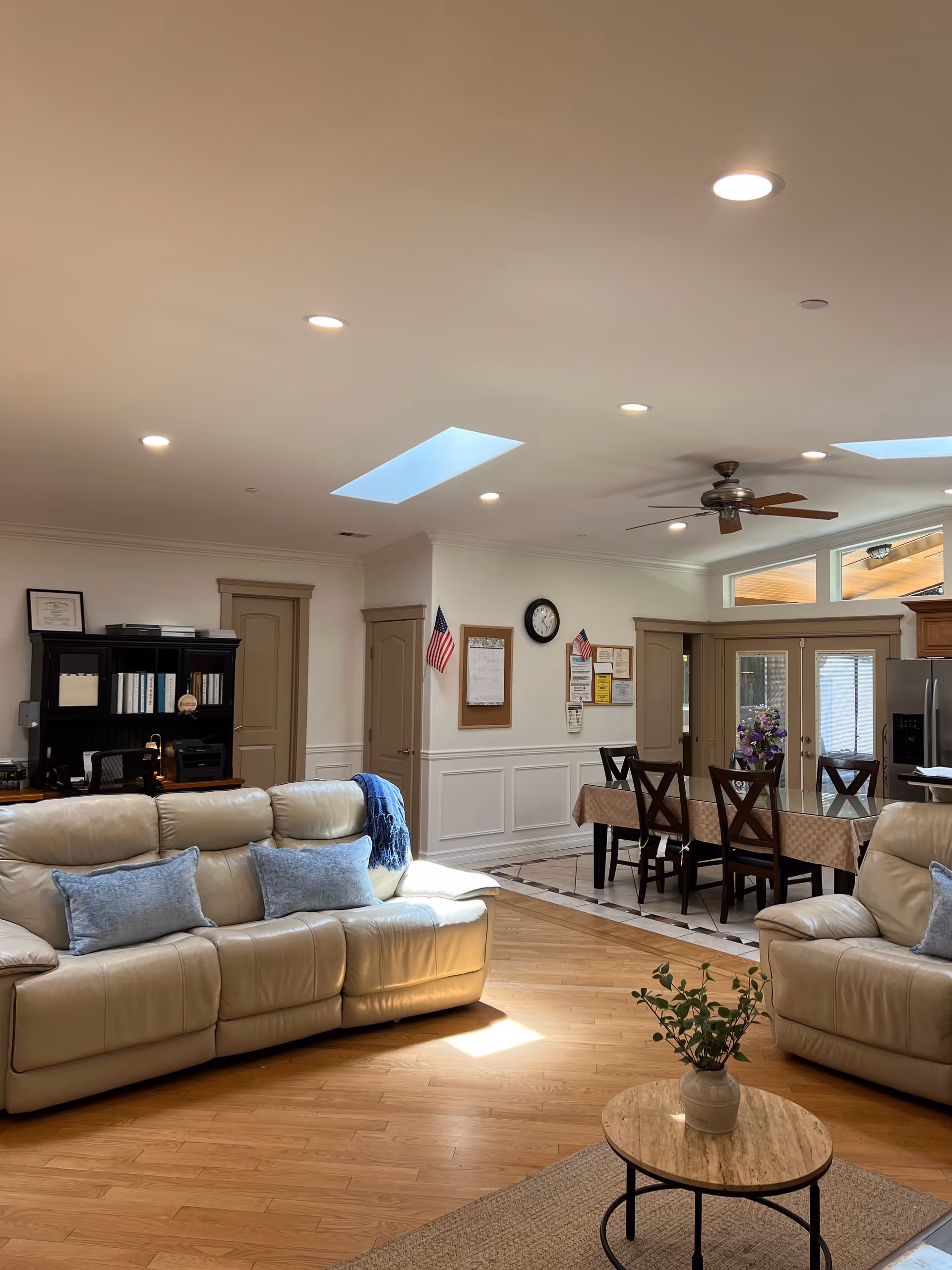 Spacious living area with beige leather sofas, a dining table, skylights, and a ceiling fan.