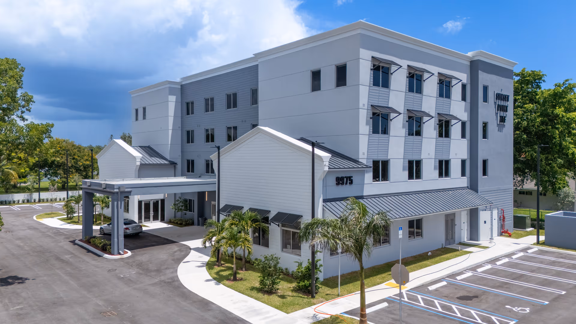 Exterior view of Sunset Point ALF, a modern white, four-story senior living facility with entrance canopy.