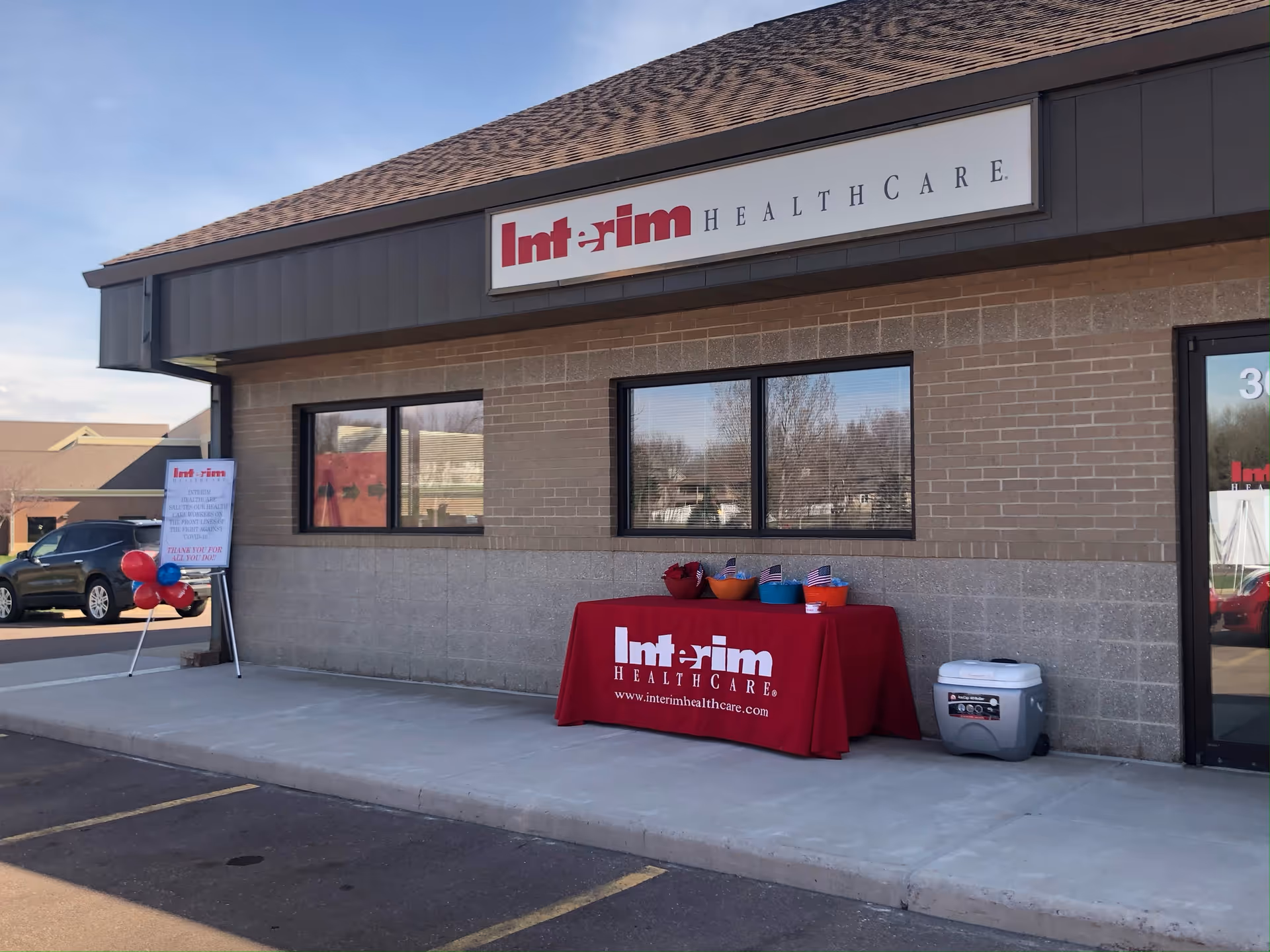 Exterior view of Interim HealthCare building with a red table and balloons outside.