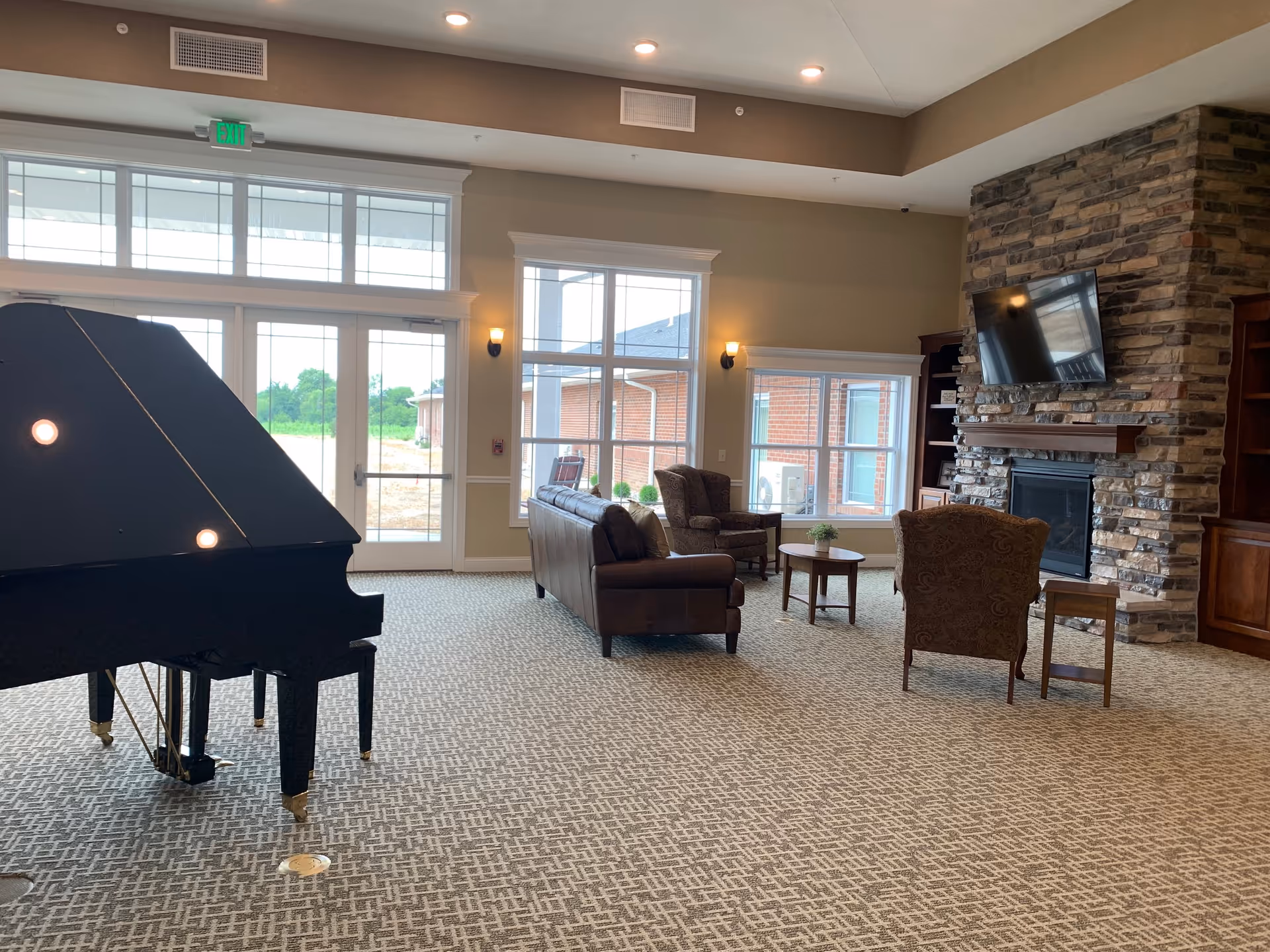 Lobby-style living room with a grand piano, sofas, a fireplace, and large windows.
