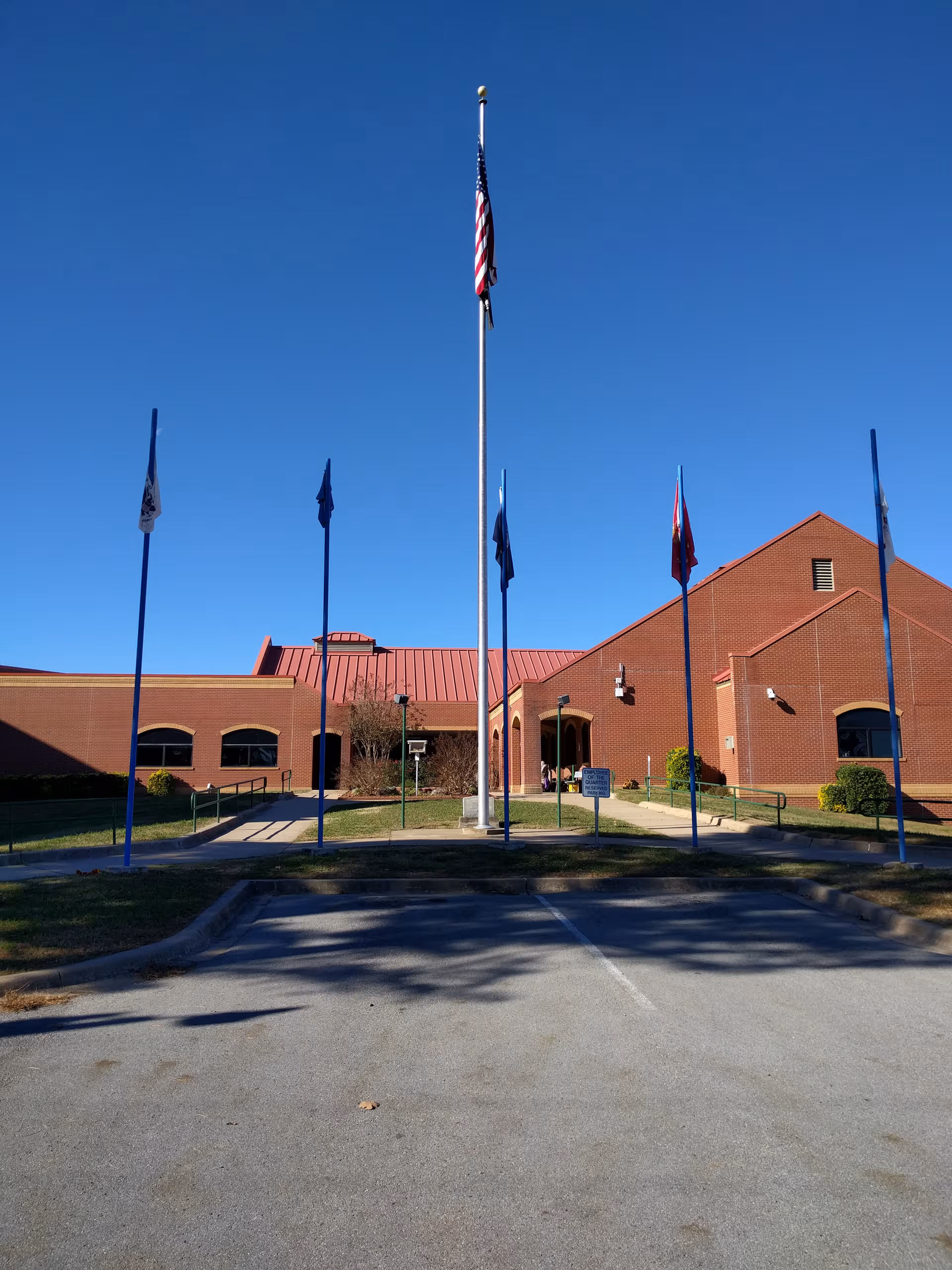 Brick building with flagpoles in front and a central entrance under a clear blue sky.