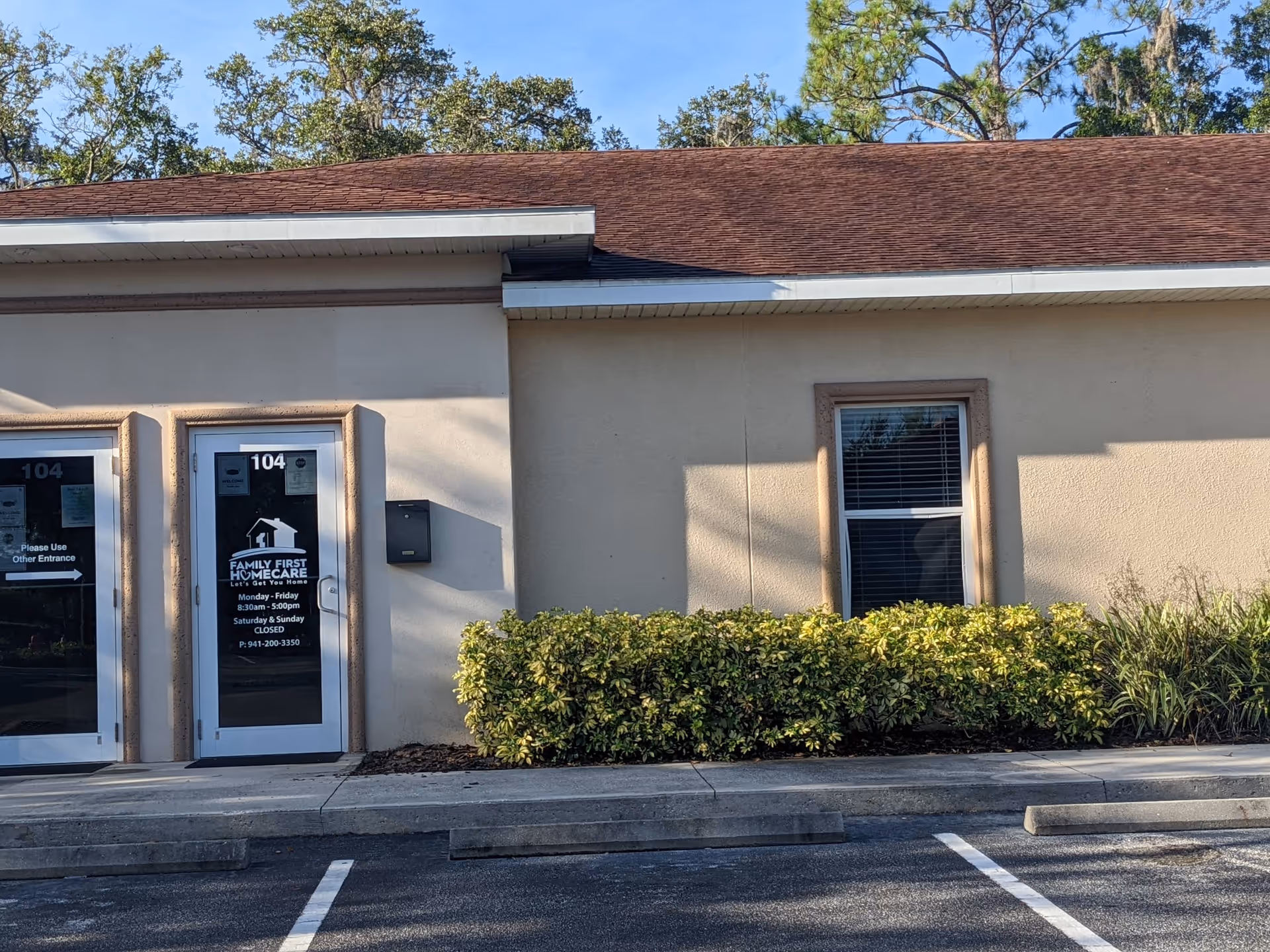 Exterior view of a single-story beige building with entry doors labeled 104 and landscaping in front.