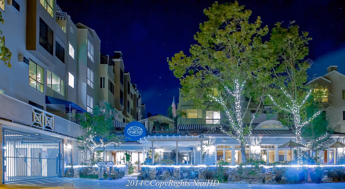 Night view of The Heritage Downtown entrance with trees wrapped in lights and illuminated building facade.