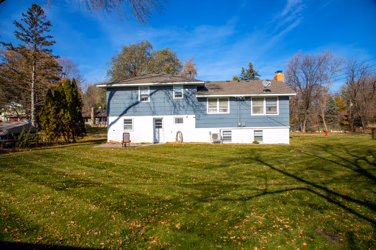 Blue two-story house with white foundation sits on a grassy yard under a clear blue sky.