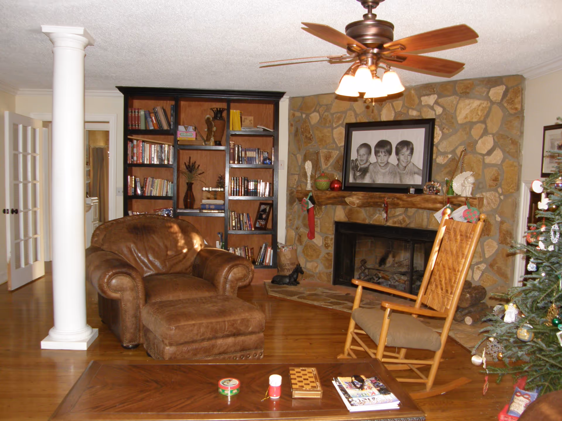 Cozy living room with a leather armchair and ottoman, rocking chair, bookshelf, and a stone fireplace with a mantle.