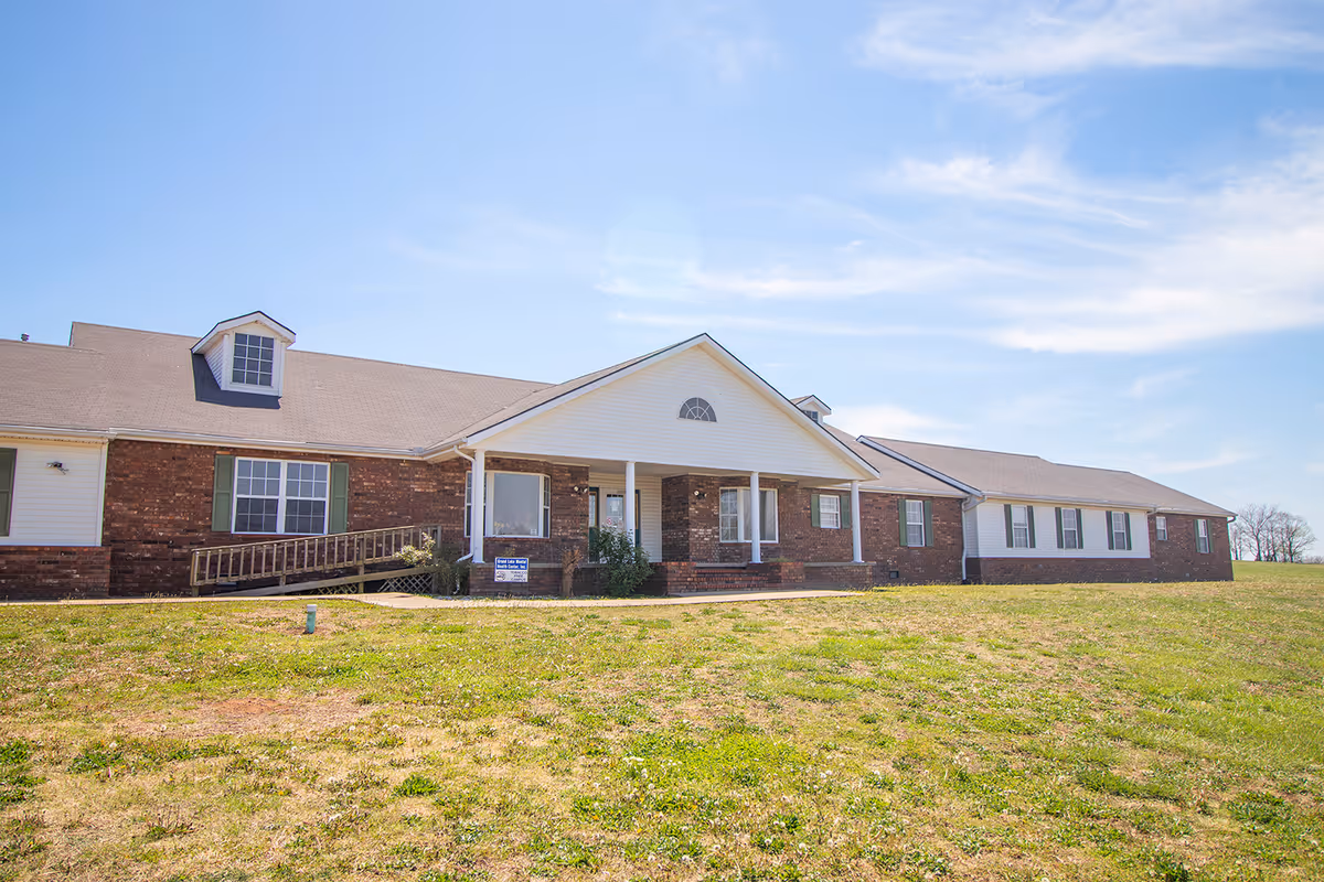 Brick senior living facility with a covered entrance and ramp, under a blue sky.