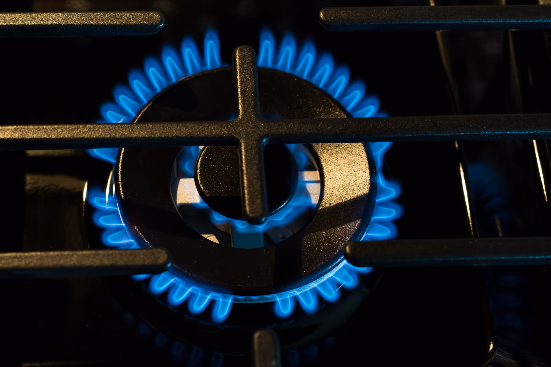 Close-up view of a gas stove burner with a blue flame burning around the circular burner grate.