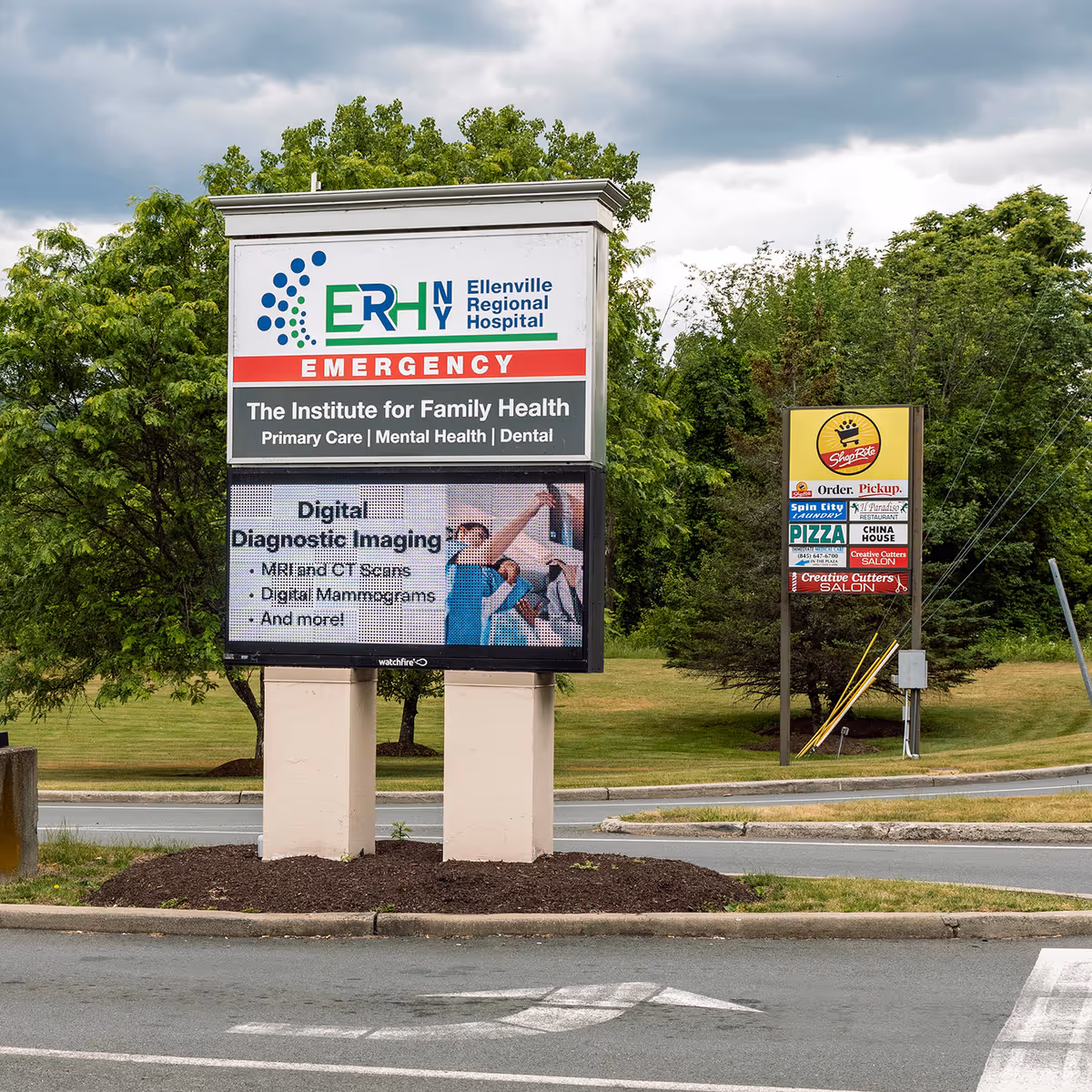 Hospital exterior sign for Emergency services on a pedestal beside a parking lot.