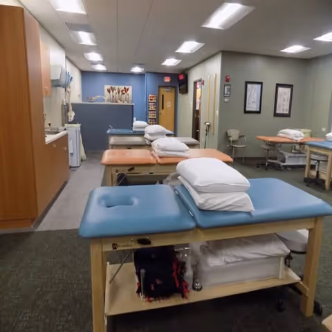 Interior therapy room with several treatment tables, pillows, and medical equipment.