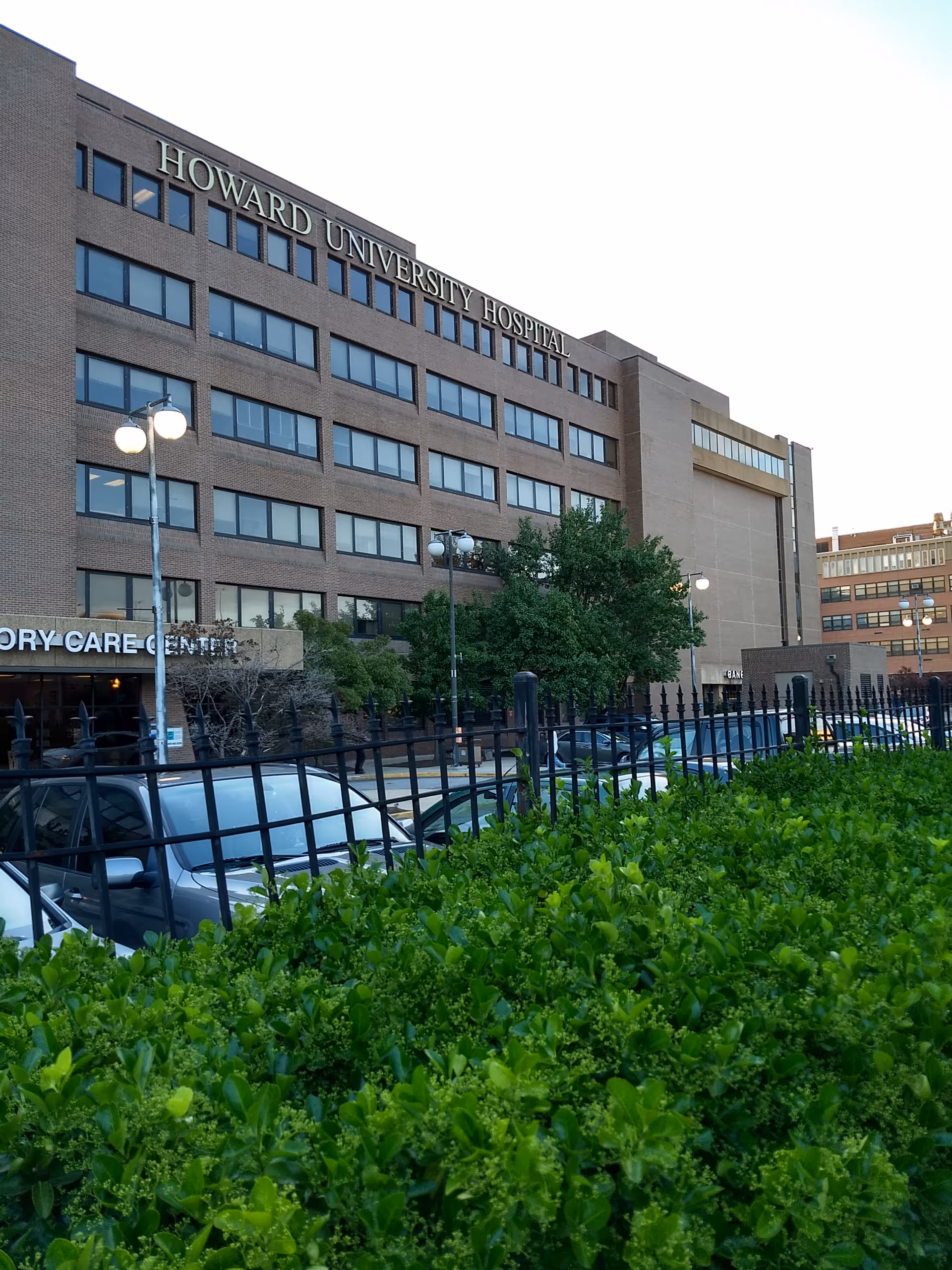 Front view of Howard University Hospital building with parked cars and green shrubs in foreground.