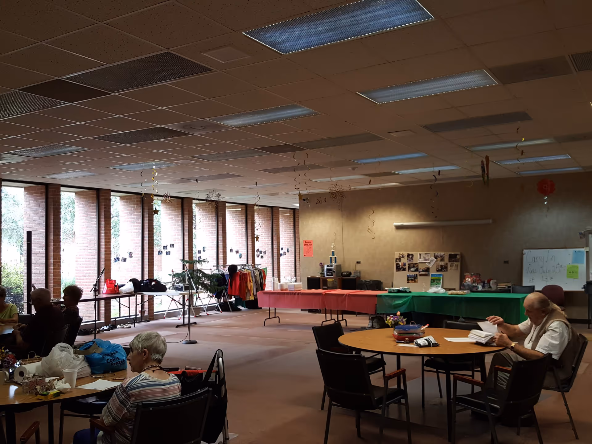 Indoor community room with elderly residents seated at tables and event decorations.