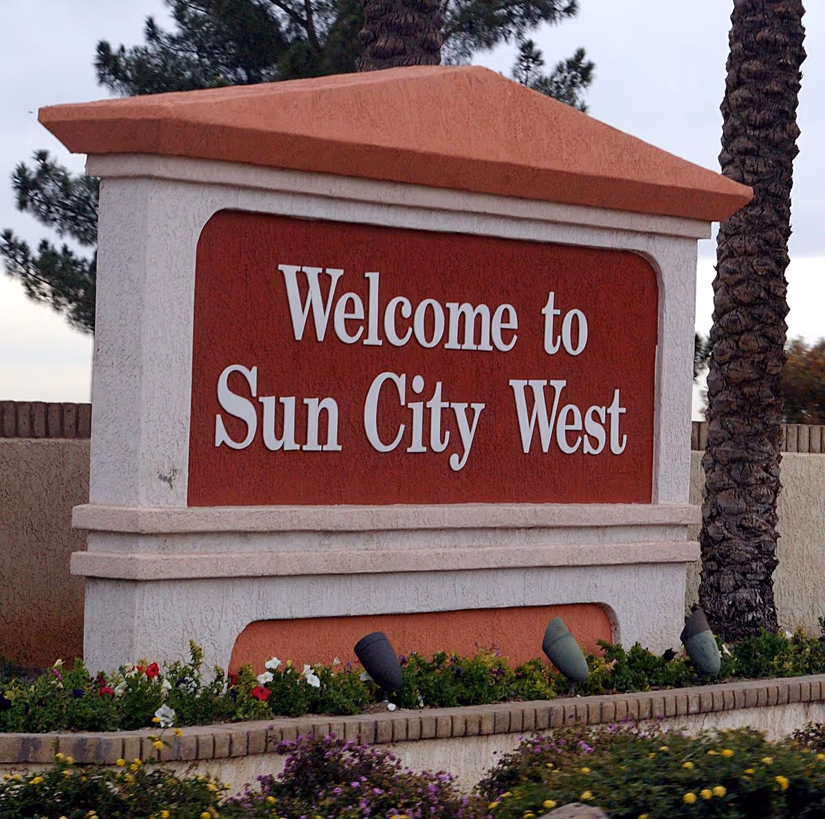 Welcome to Sun City West sign with landscaping and palm trees.