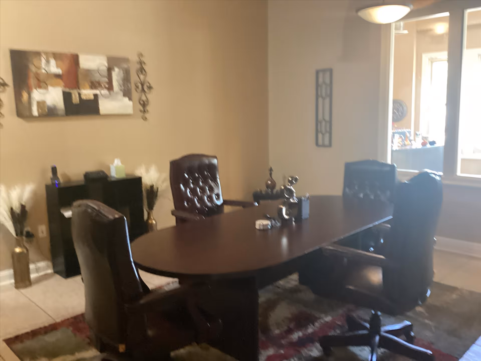 Office conference area with dark wood desk, plush chairs, wall art, and window light.