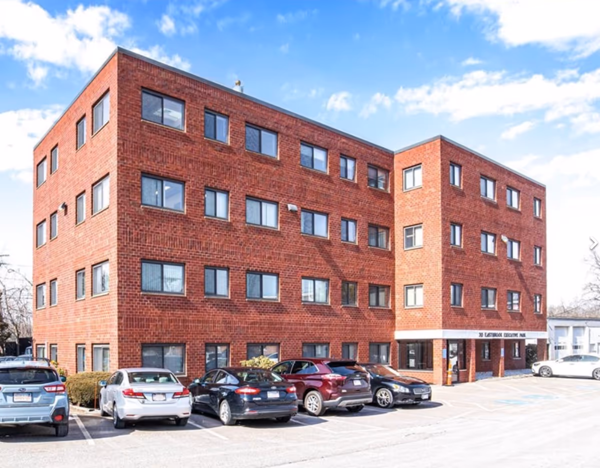 Exterior view of a red brick, three-story senior living building with a parking lot.
