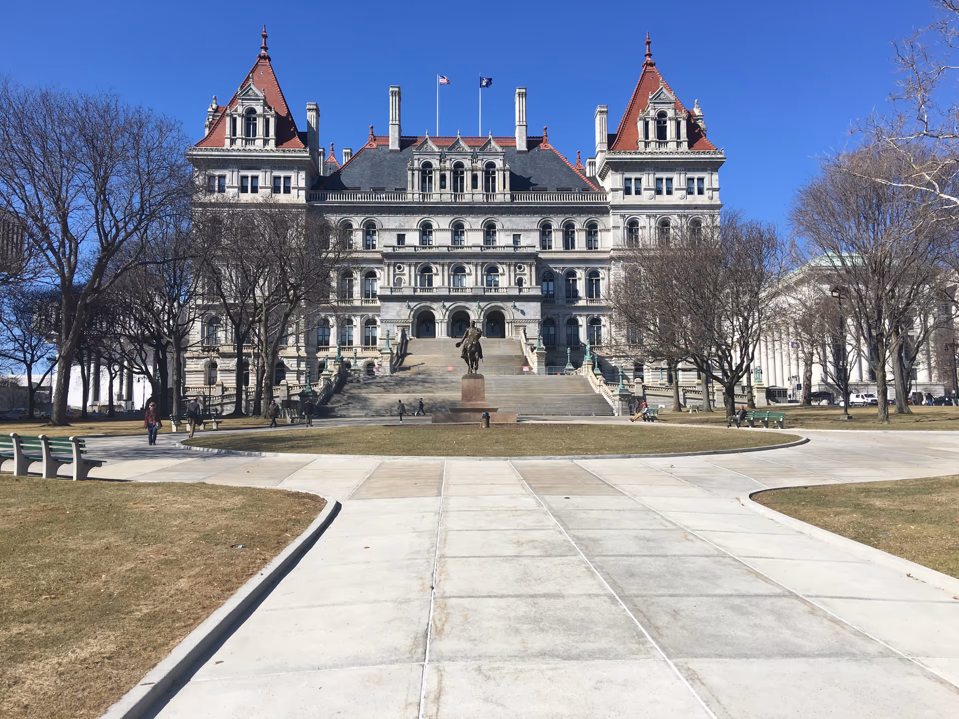 A grand historic government-style building with stairs, a statue, leafless trees, and a central plaza.