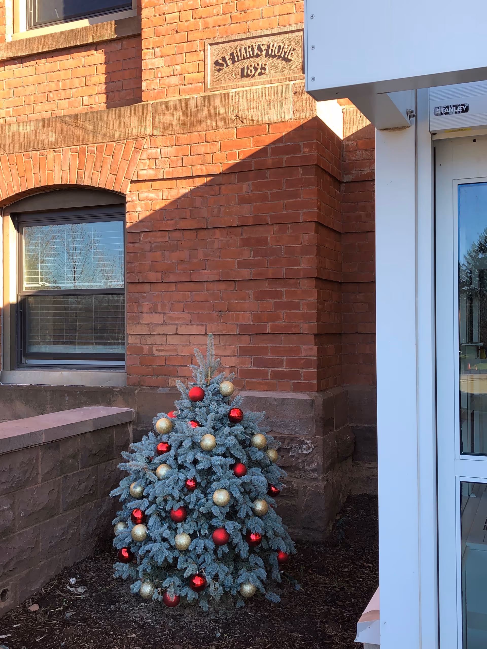 Brick building front with St. Mary's Home plaque and decorated Christmas tree.