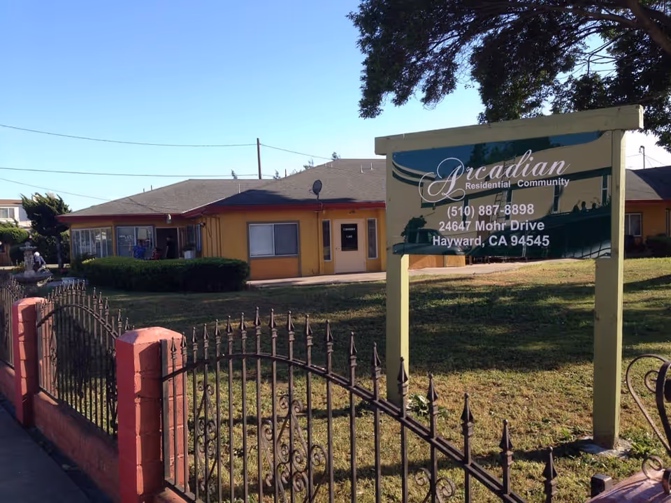 Sign for Arcadian Residential Community on a lawn in front of a single-story yellow residential building and decorative iron fence.