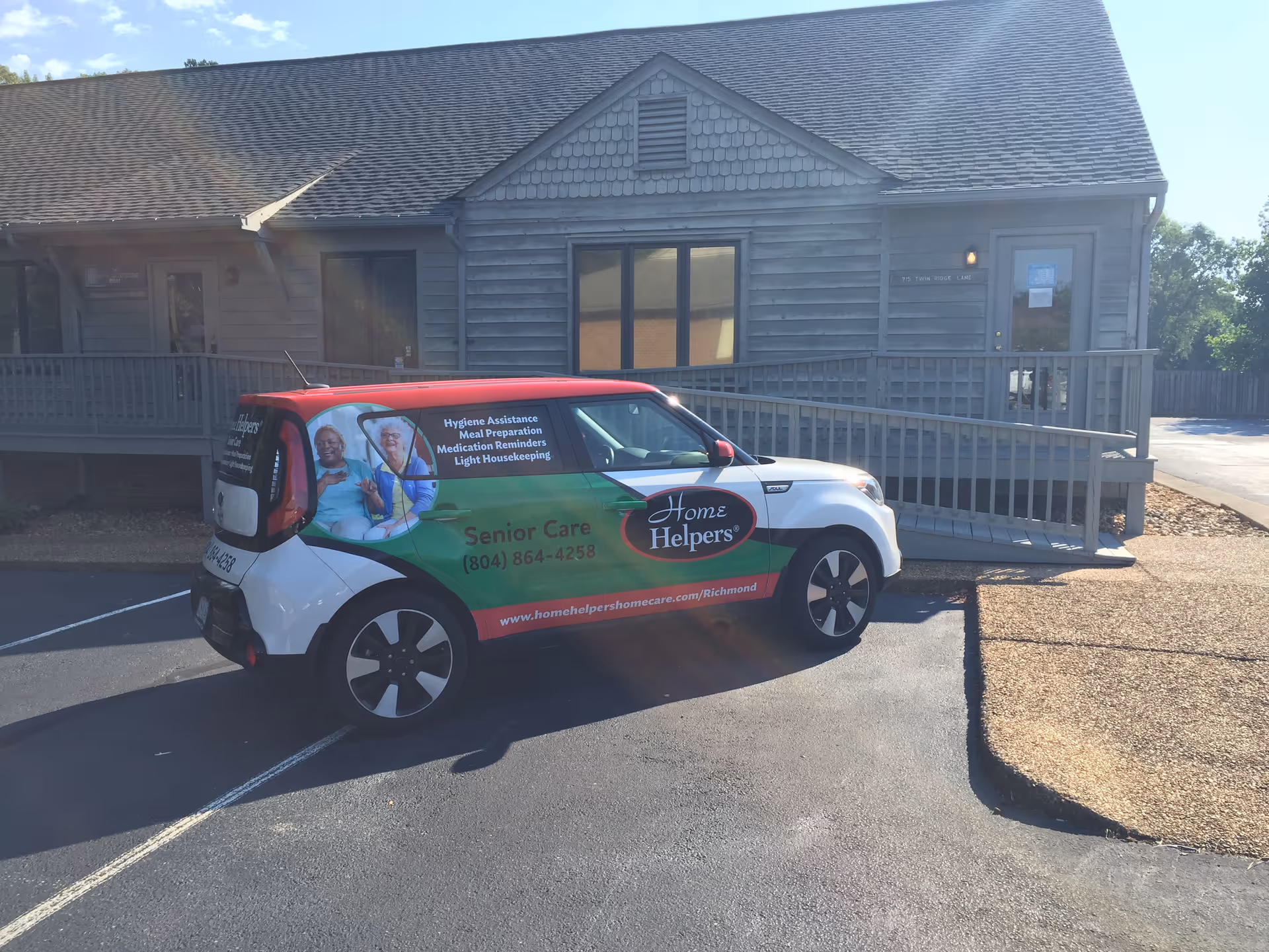 Exterior of a gray wooden building with a branded Home Helpers car in the parking lot.