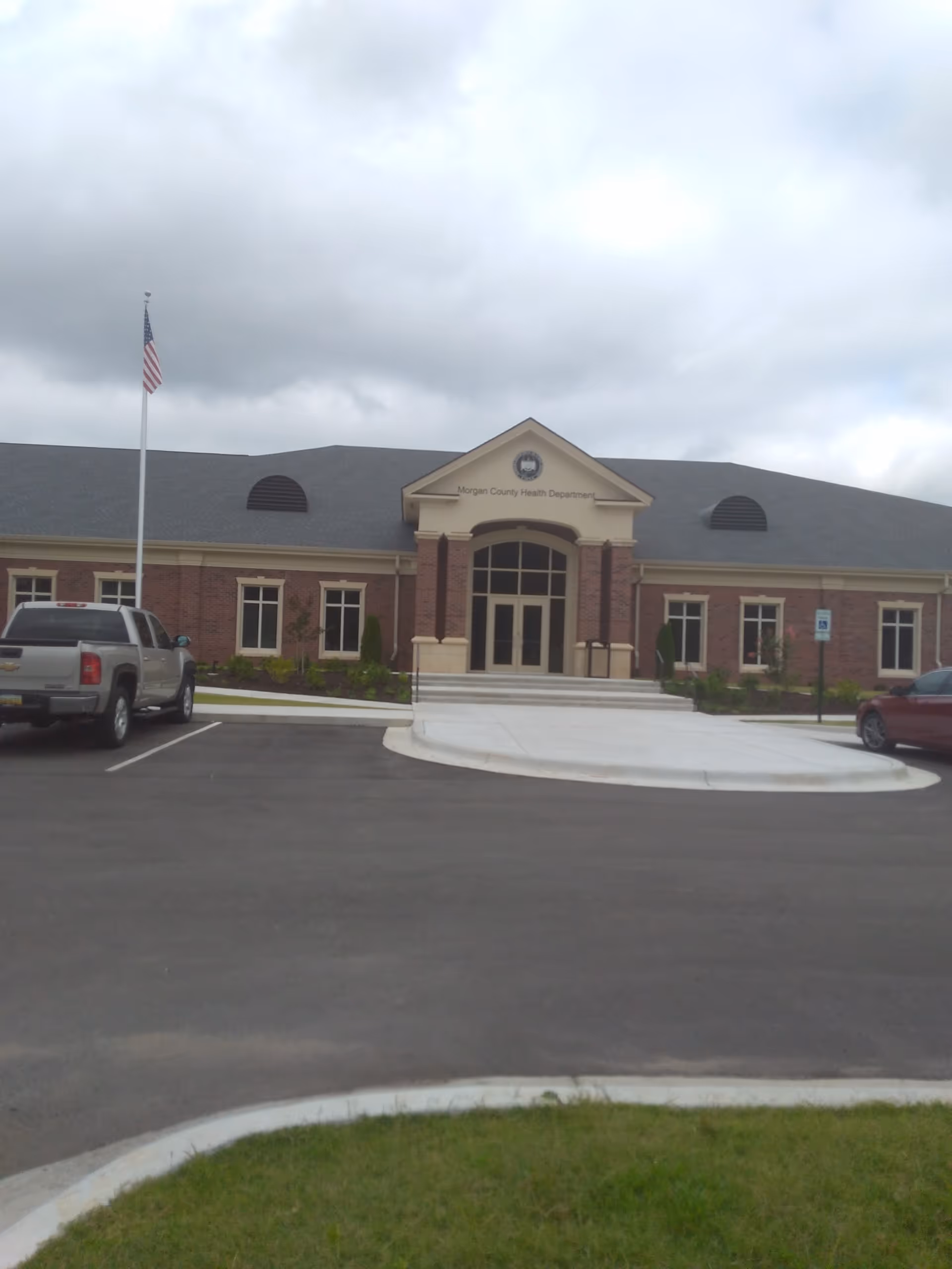 Front view of Morgan County Health Department building with entrance, flagpole, and parked cars.