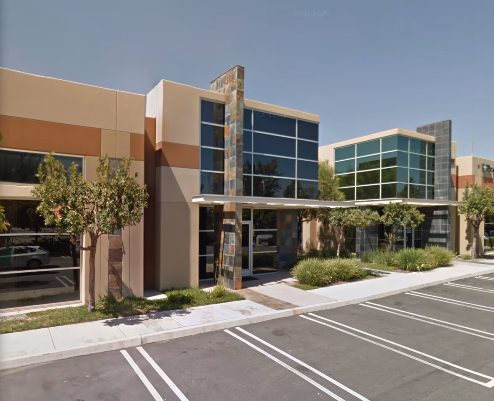Modern single-story building with large glass windows, stone columns, and landscaped entrance.