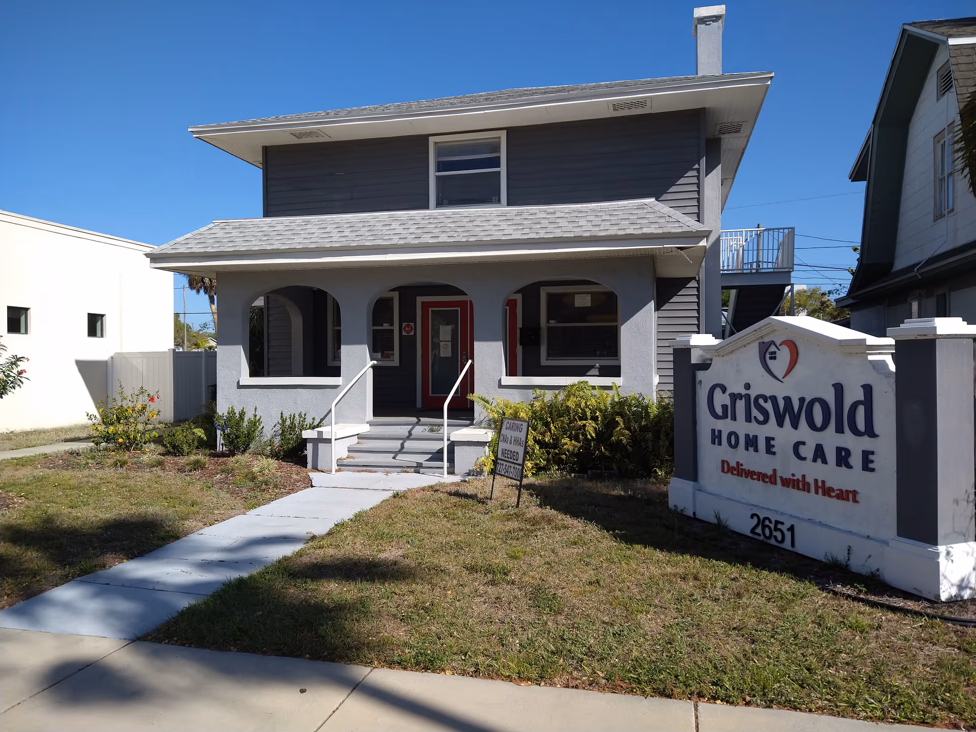 Two-story gray building with a sidewalk, entrance stairs, and Griswold Home Care sign.