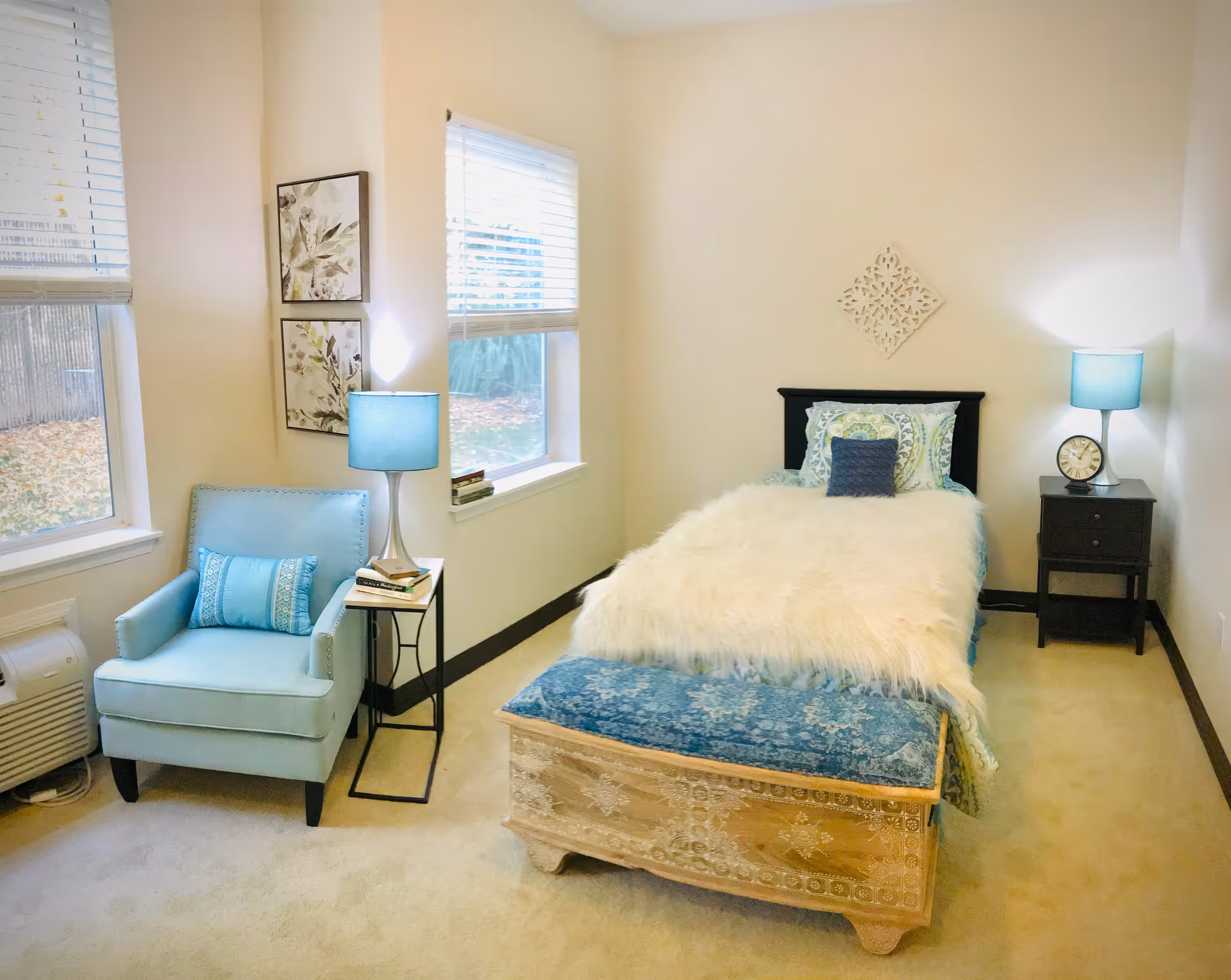 A cozy bedroom with a blue chair, nightstands, lamps, and a fur blanket on the bed.