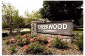 Creekwood Apartments sign in front of landscaped flower beds and trees.