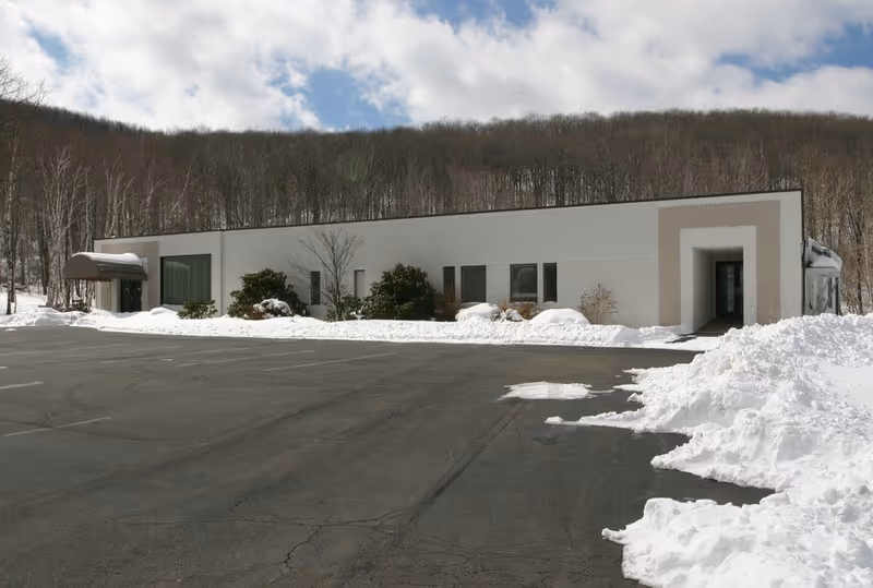 Snow-covered, single-story building with a long white facade and plowed parking lot.