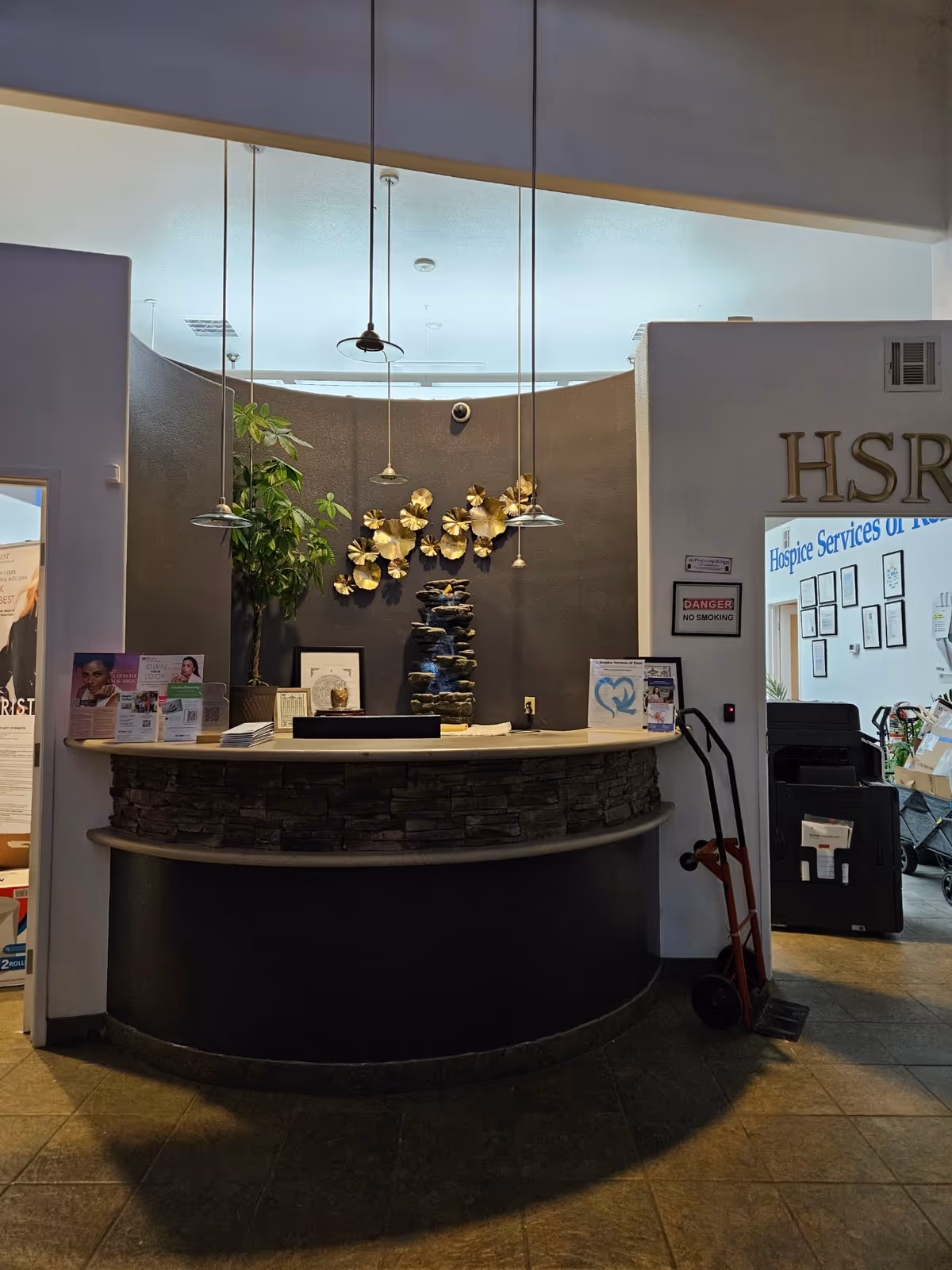 Reception desk with stone facade in hospice lobby featuring plants and wall art.