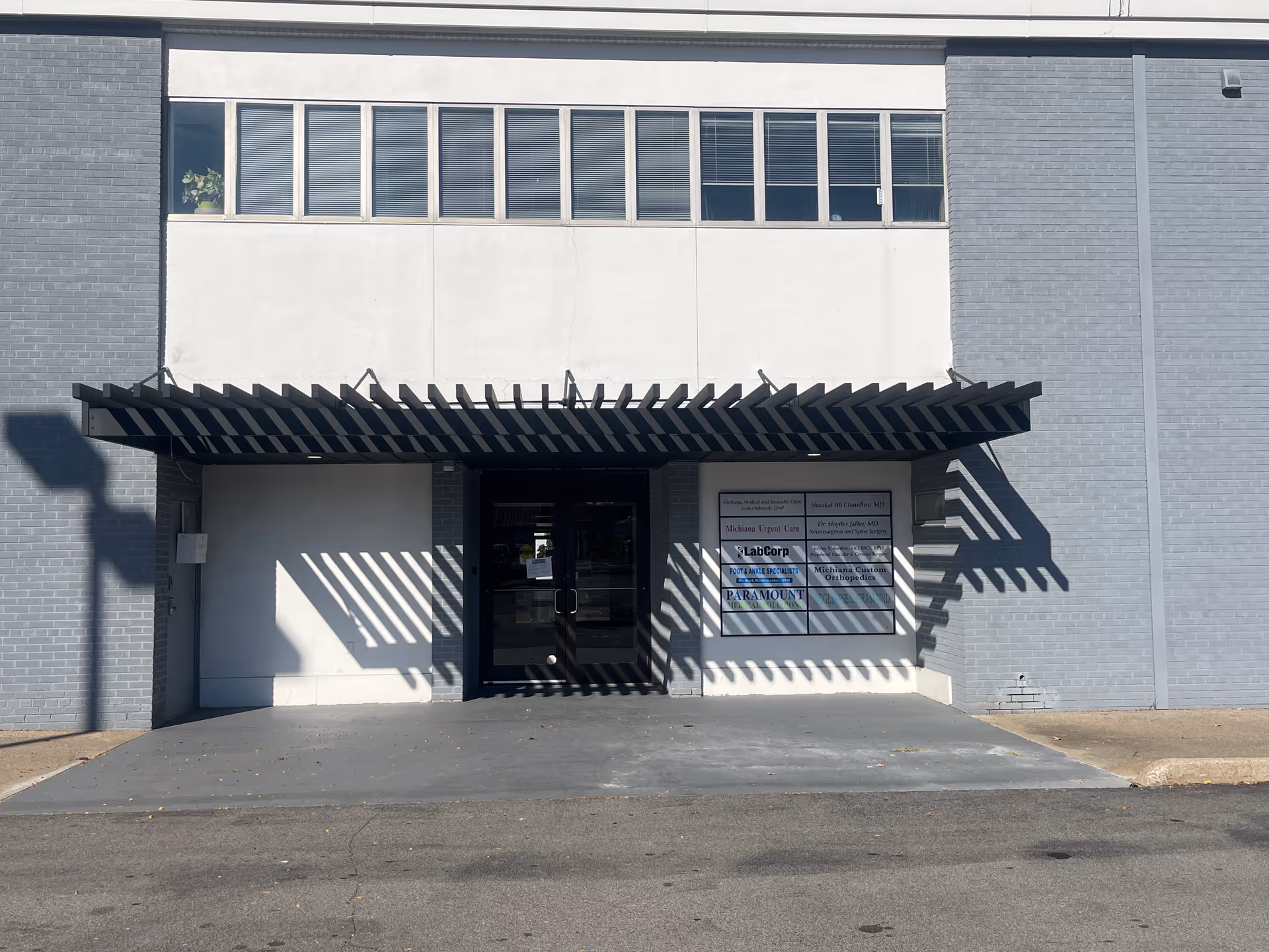 Modern building entrance with a metal slatted awning casting striped shadows.