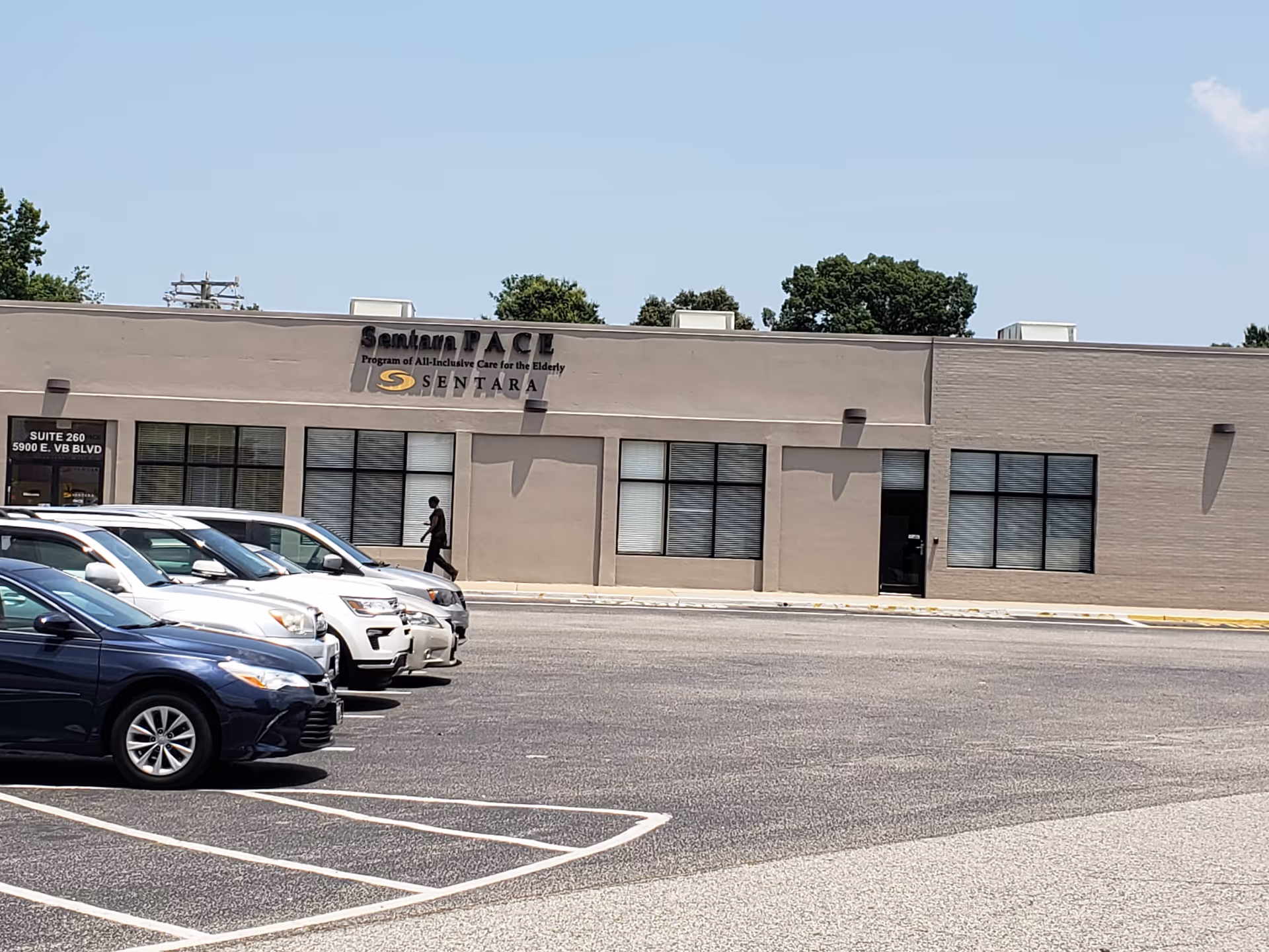 Exterior view of Sentara PACE building with cars in parking lot and a person walking.