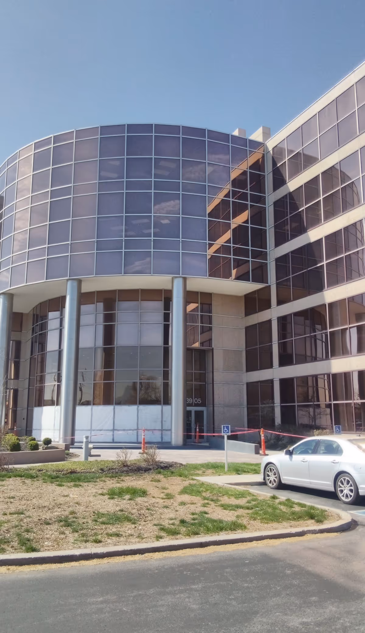 Modern glass-fronted senior living facility with curved entrance and a parked car in the foreground.