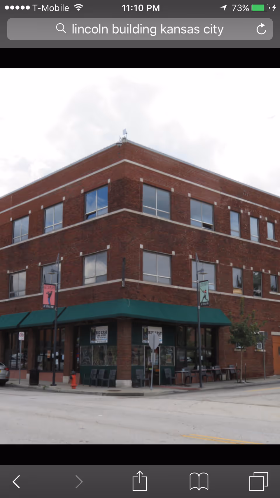Three-story brick building on a street corner with green awning storefronts and outdoor seating.