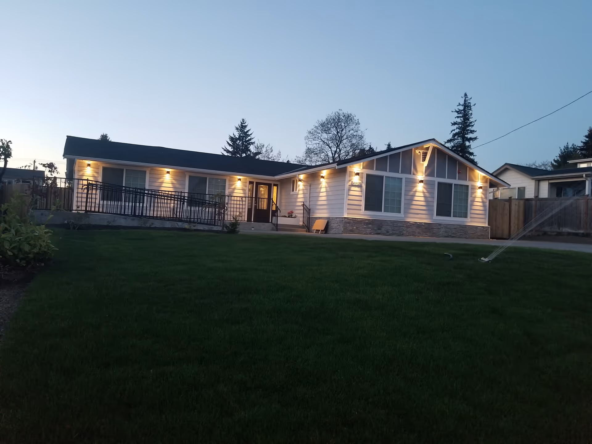 A single-story adult care home exterior with lit windows and a green front lawn.