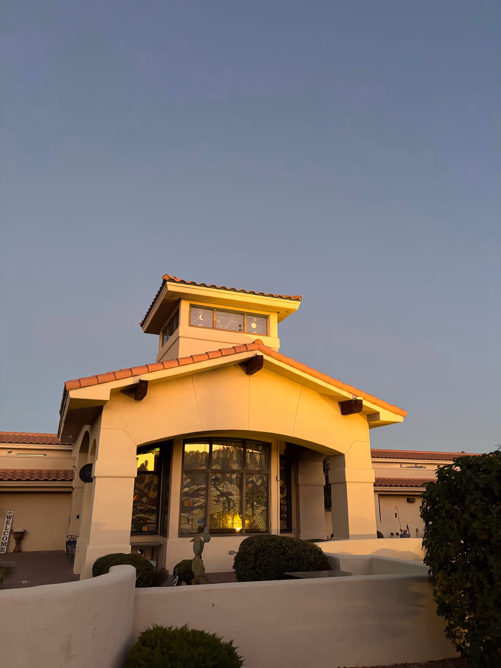 A tan stucco building with red tiled roof and a tall tower, against a clear sky.