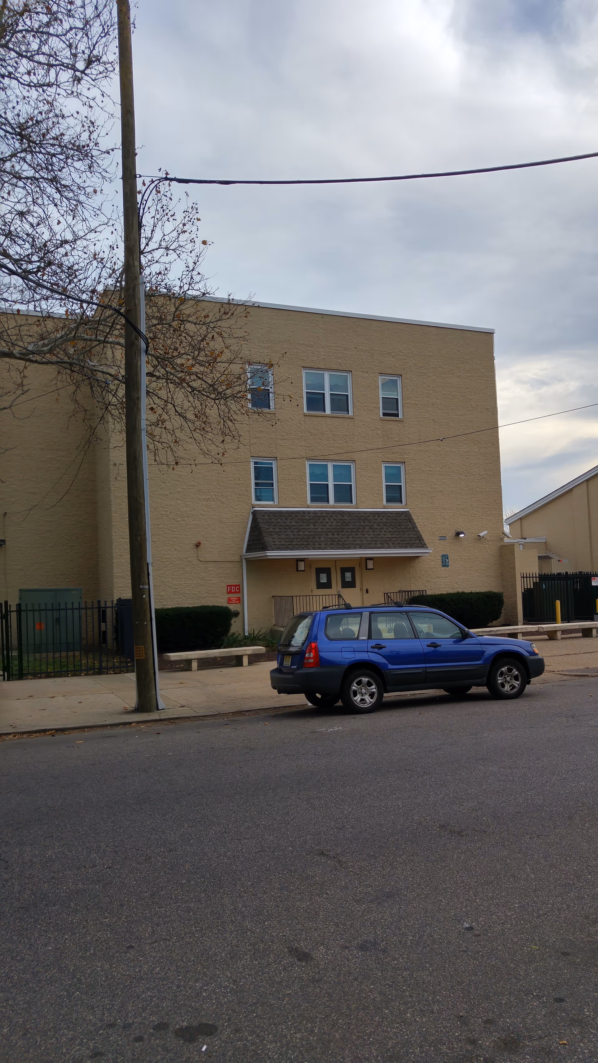 Exterior of a beige multi-story building with a blue SUV parked on the street.